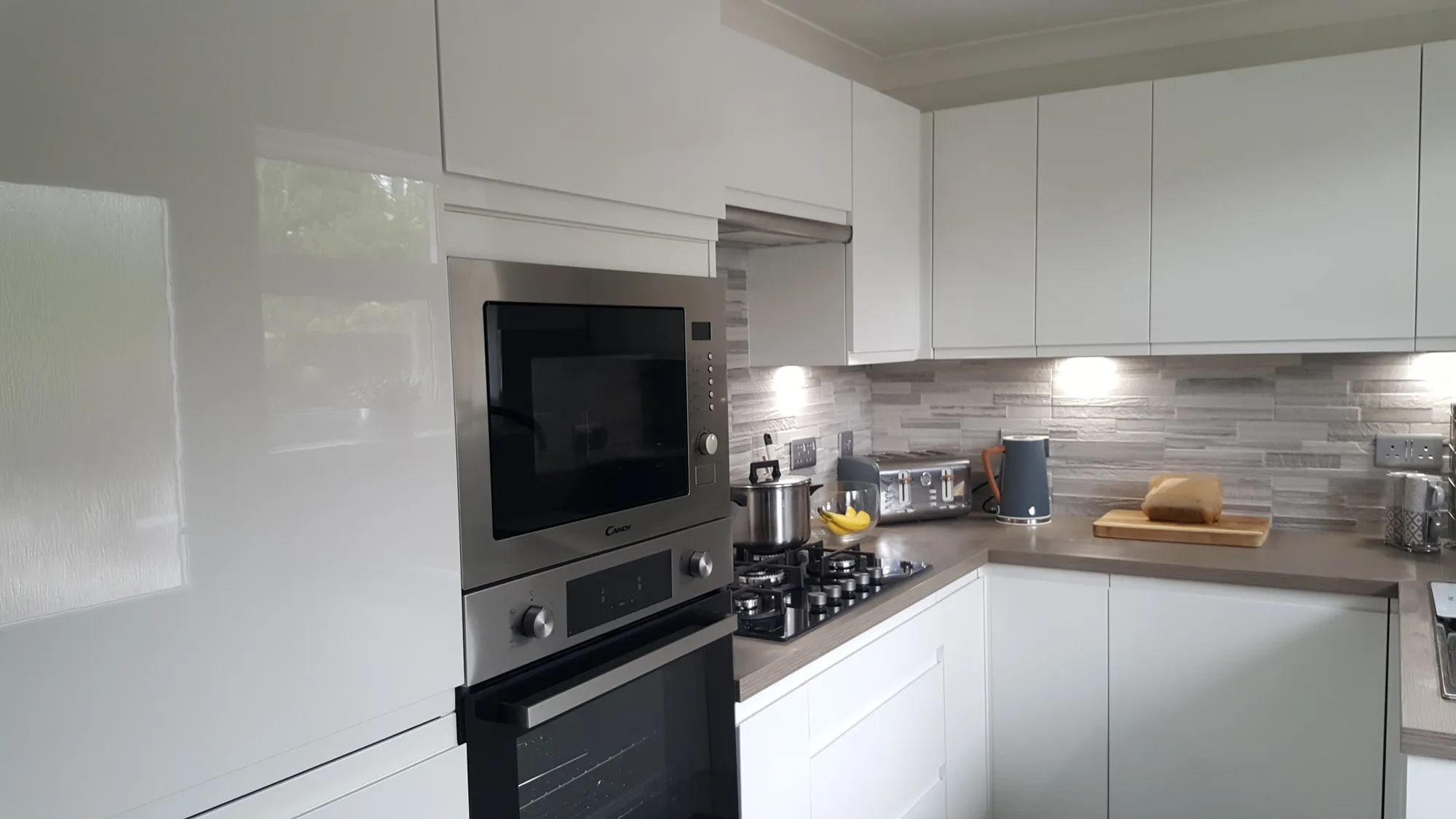 Raised Candy oven and microwave beside the gas hob in the white handleless Glasgow kitchen