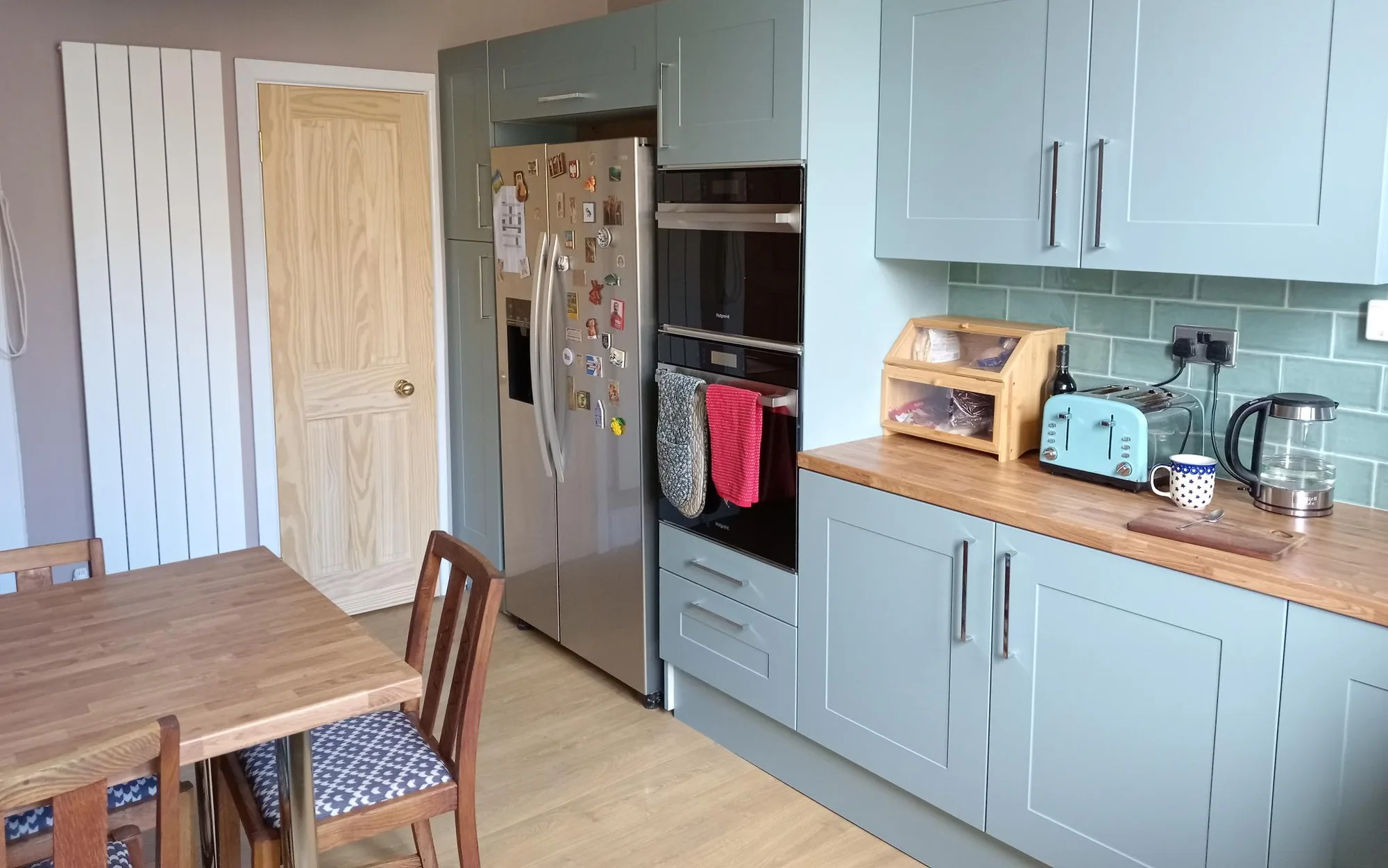 Tall housing with the oven and microwave raised to working height beside an American fridge freezer in the duck egg shaker kitchen