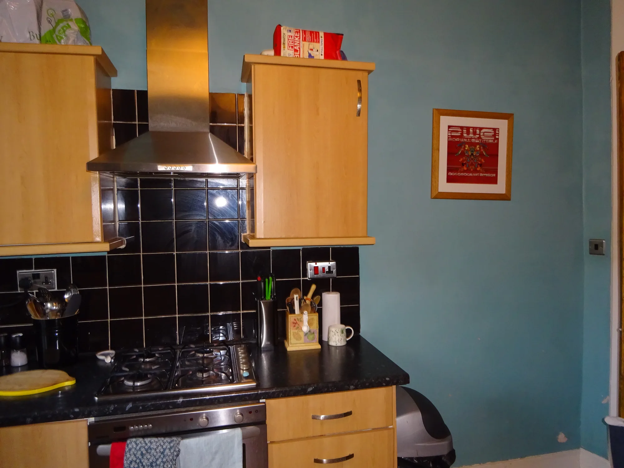 The old beech kitchen before renovation, with black gloss tiles and a stainless steel chimney hood over the hob
