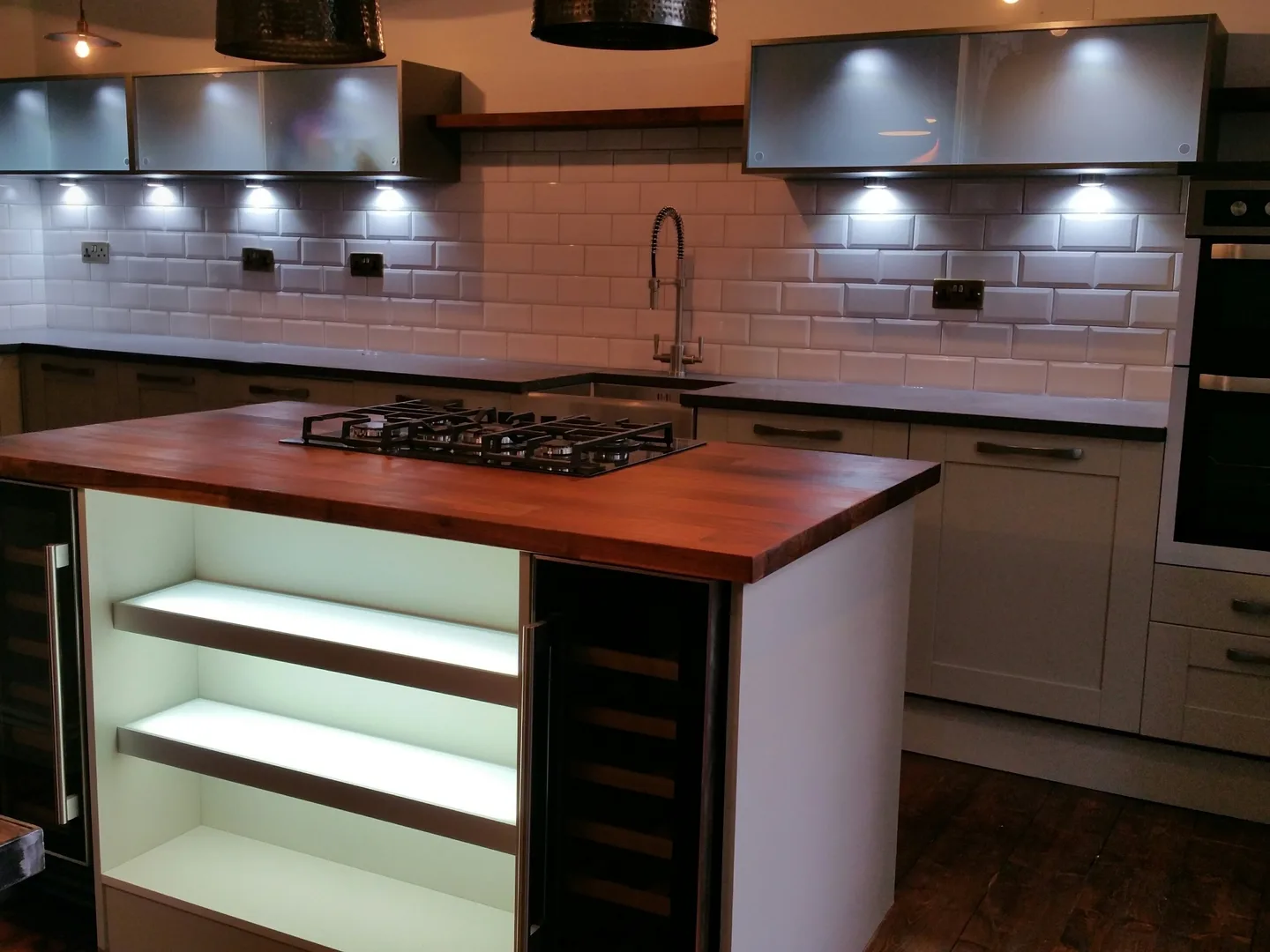 Off-white shaker kitchen in a Glasgow tenement with a timber-topped island, gas hob, wine cooler and white metro tiles under hammered pendants