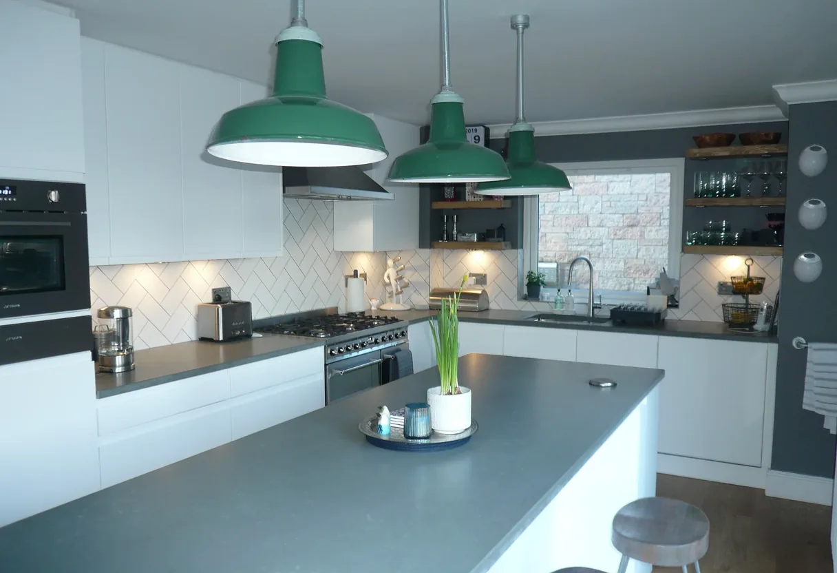White handleless kitchen with grey worktops, an island and green enamel pendant lights, fitted by Leith Kitchens in Clydebank