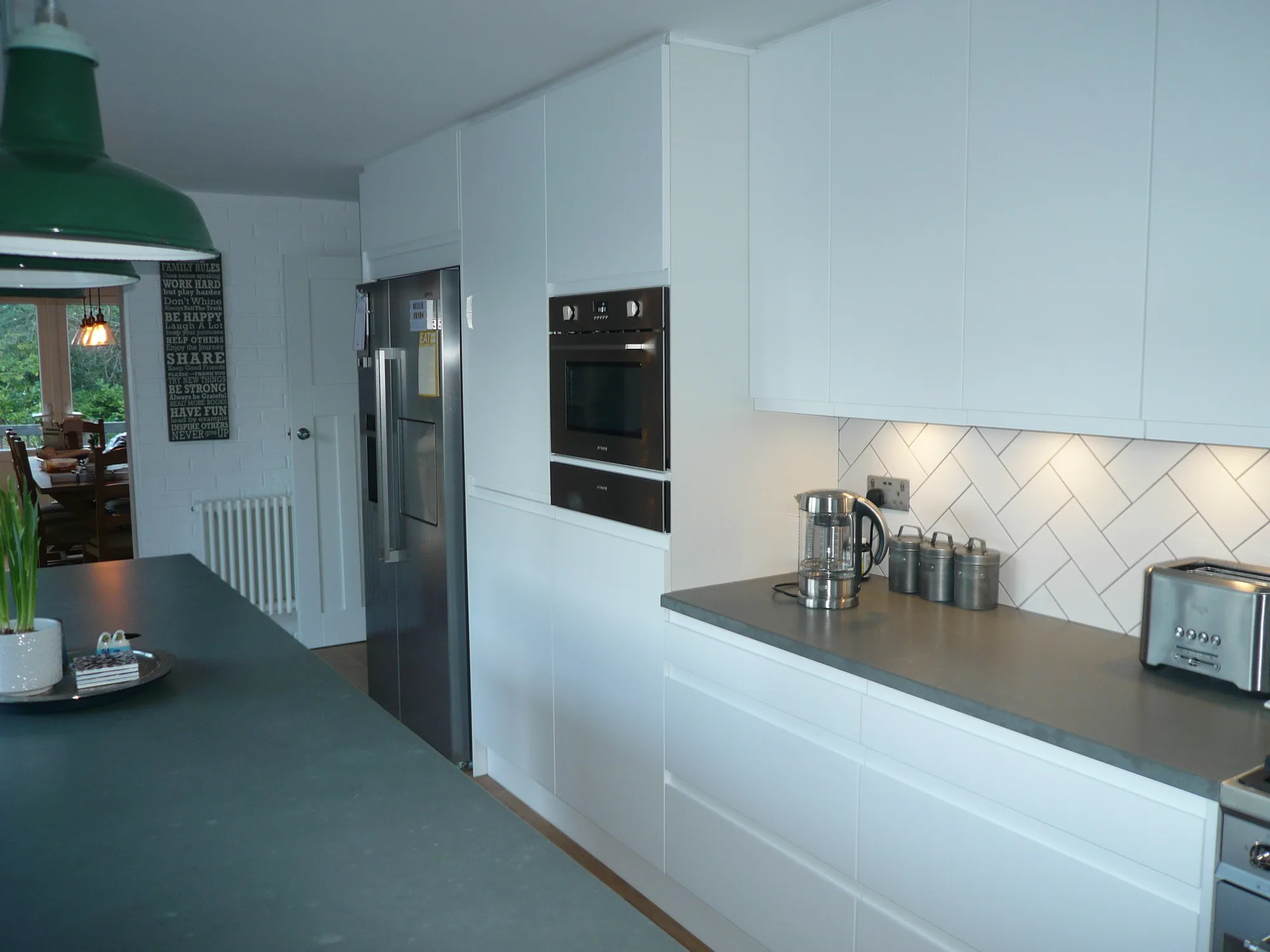 Tall bank of matt white handleless units housing the American fridge freezer and built-in microwave