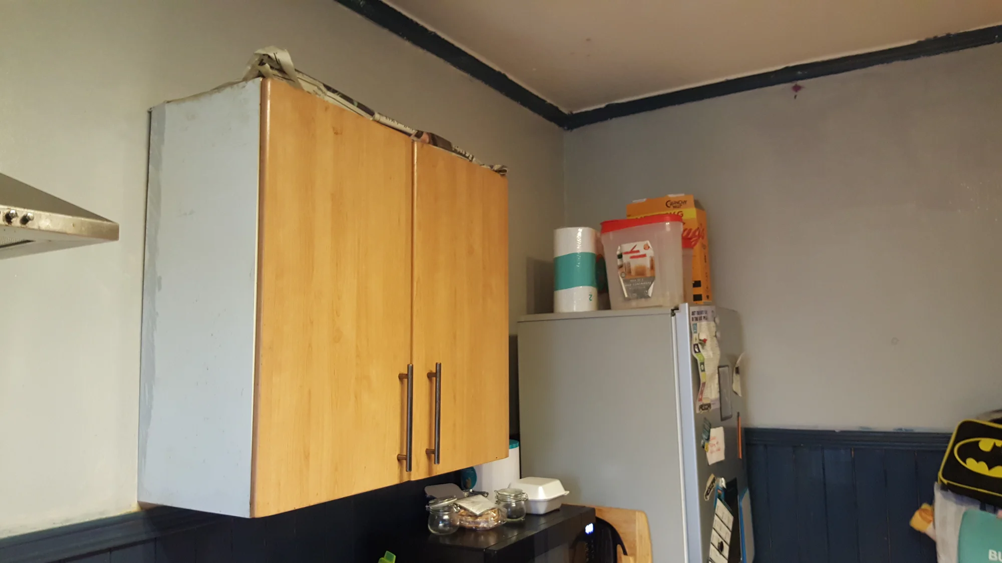 Old beech-effect wall cupboard with newspaper stuffed along the top, before the renovation