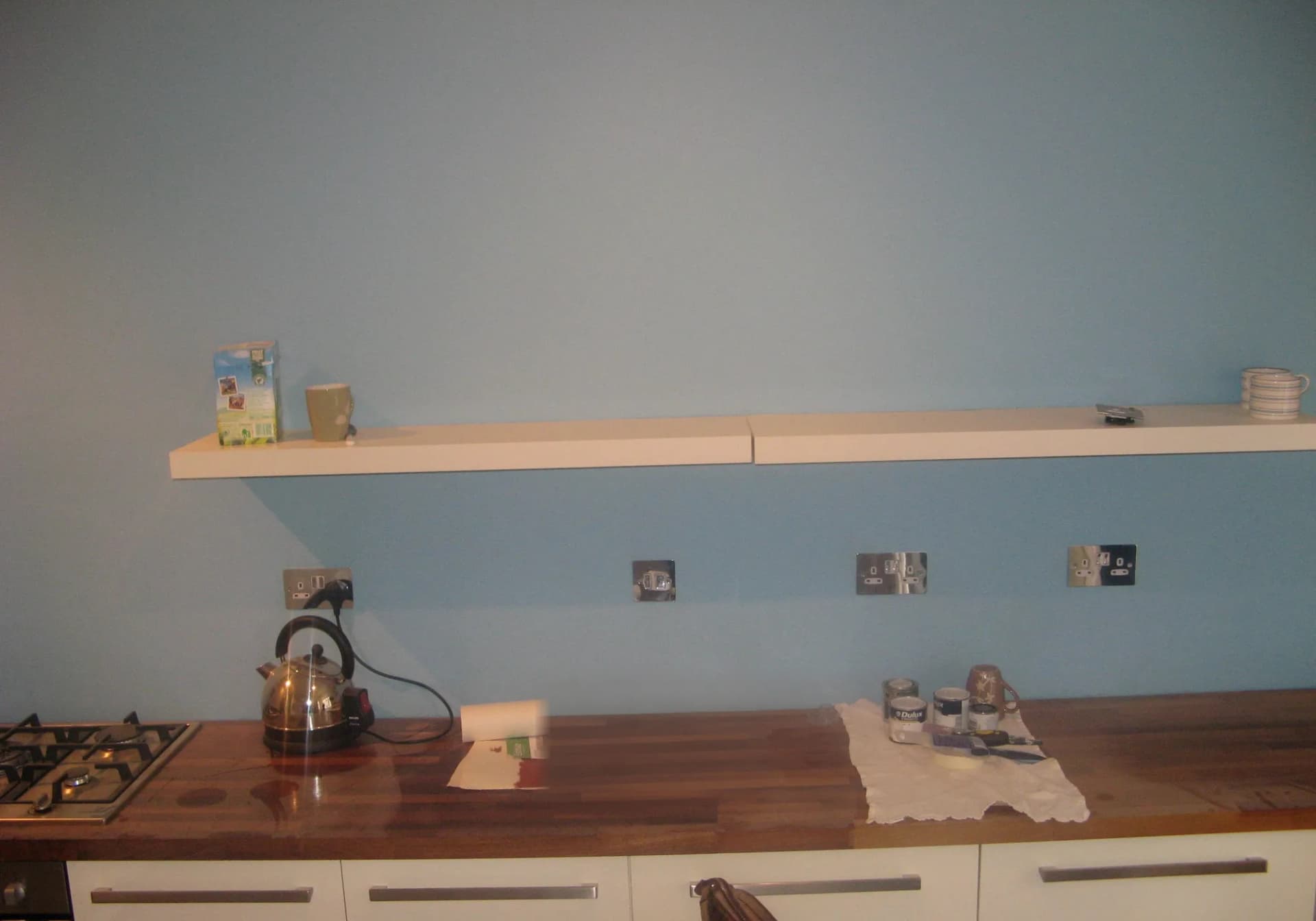The old kitchen before renovation: cream slab doors, a walnut-effect worktop, open shelves and pale blue walls