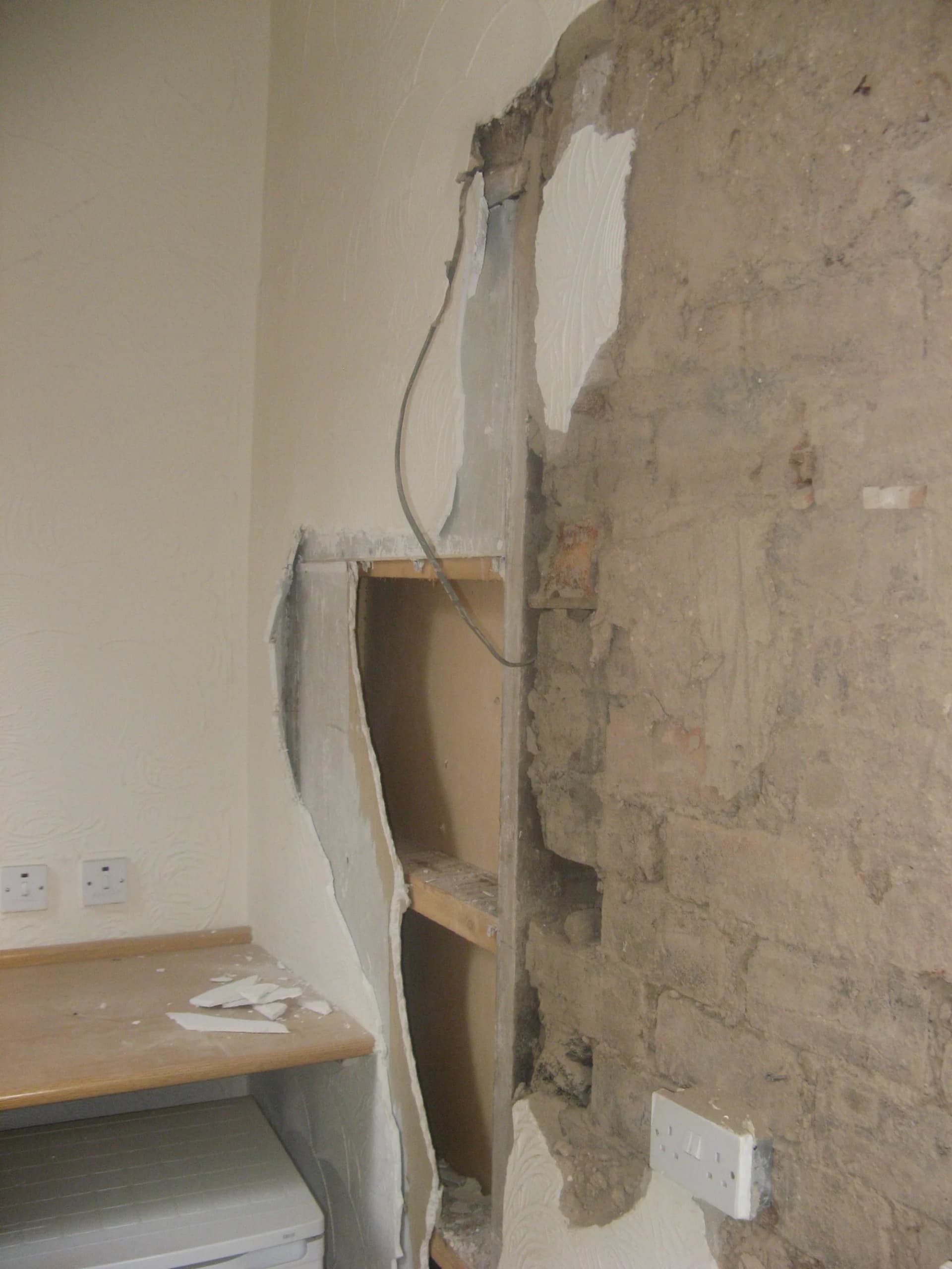 Plaster and lath stripped from a tenement kitchen wall during the renovation, exposing the rough stone behind, with a socket at skirting height